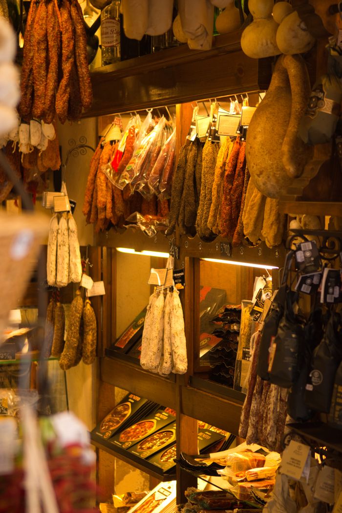 Cured meats hanging on shelves in a rustic gourmet food shop, warm ambiance.