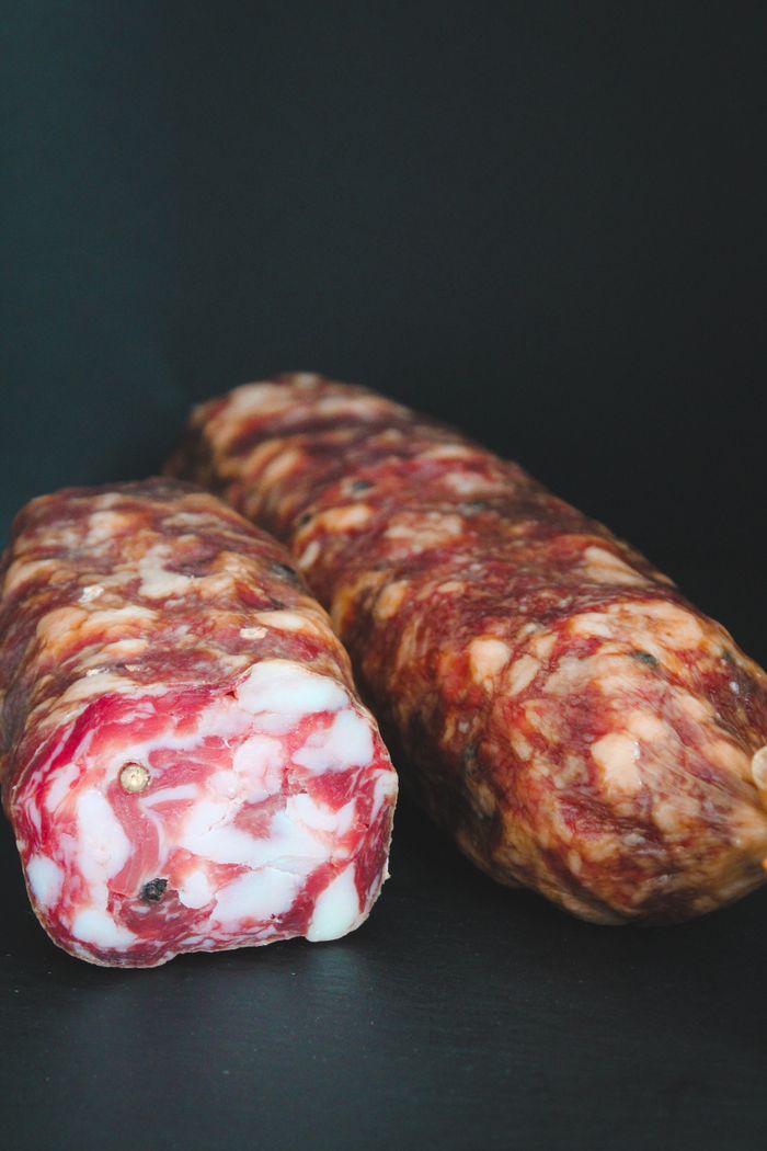 About Two rustic cured salami sticks with marbled texture on a dark surface, perfect for meat lovers.