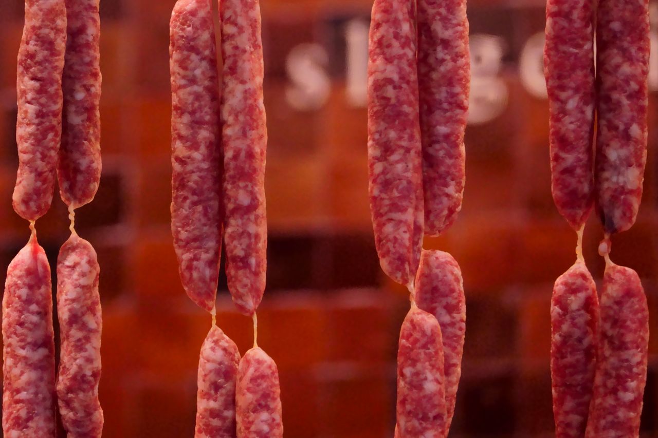 Close-up of hanging cured sausages in a traditional butcher shop setting.