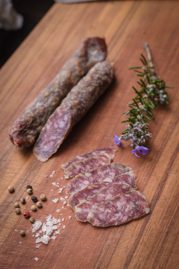 From above of tasty salami slices near sea salt and peppercorns with aromatic rosemary