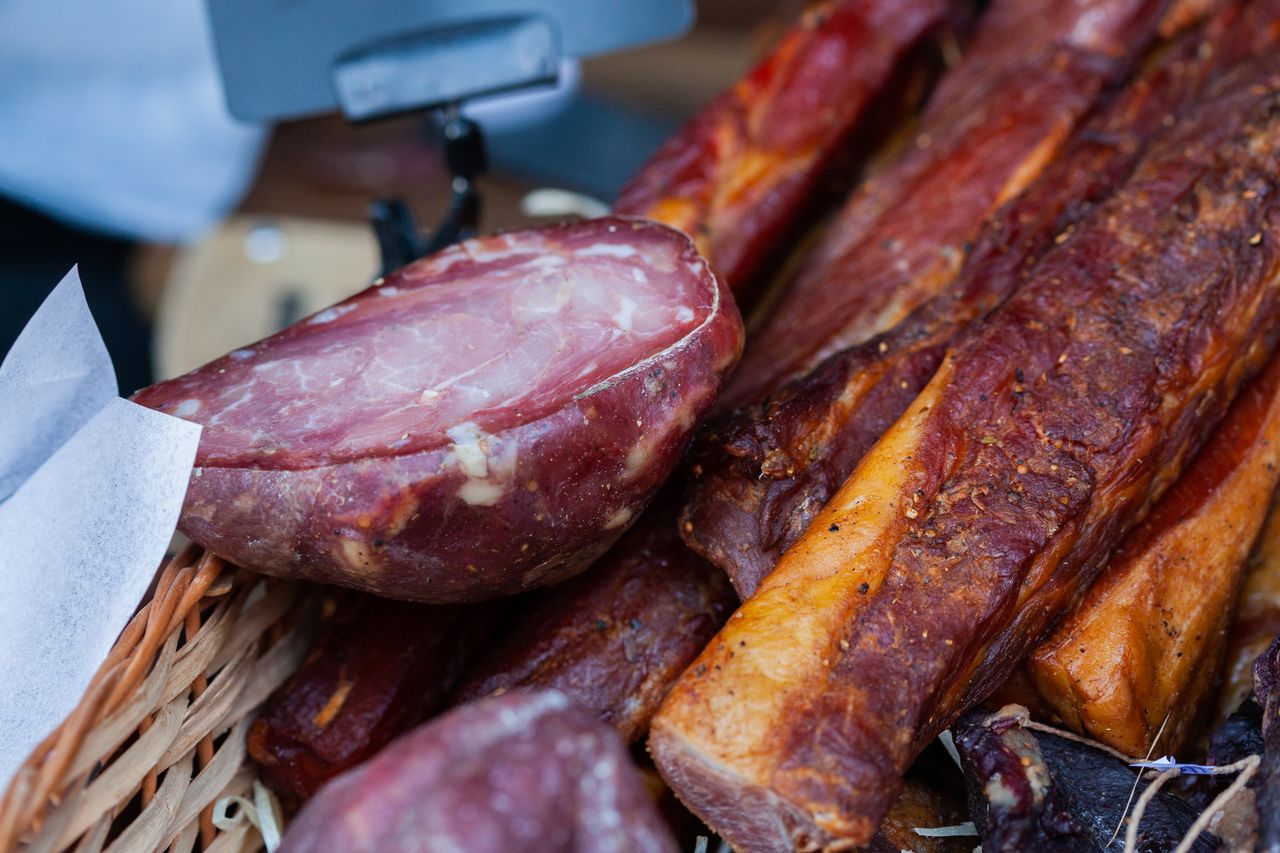 Tempting close-up of assorted smoked meats in a market basket, showcasing rich textures and flavors.